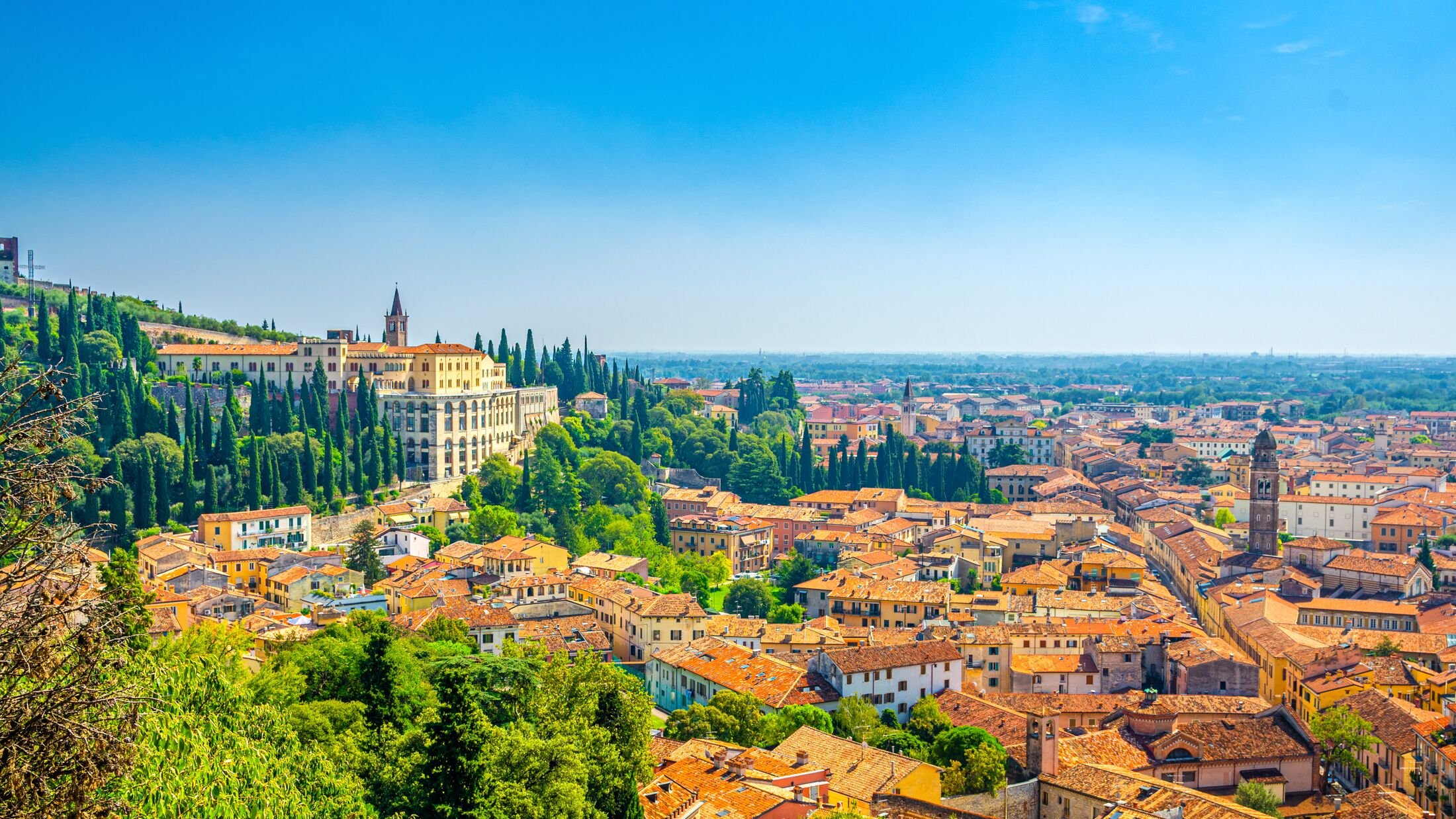 Aerial view of Verona historical city centre Veronetta, medieval buildings with red tiled roofs, cypress trees, blue sky background, Veneto Region, Italy. Verona cityscape, panoramic view.