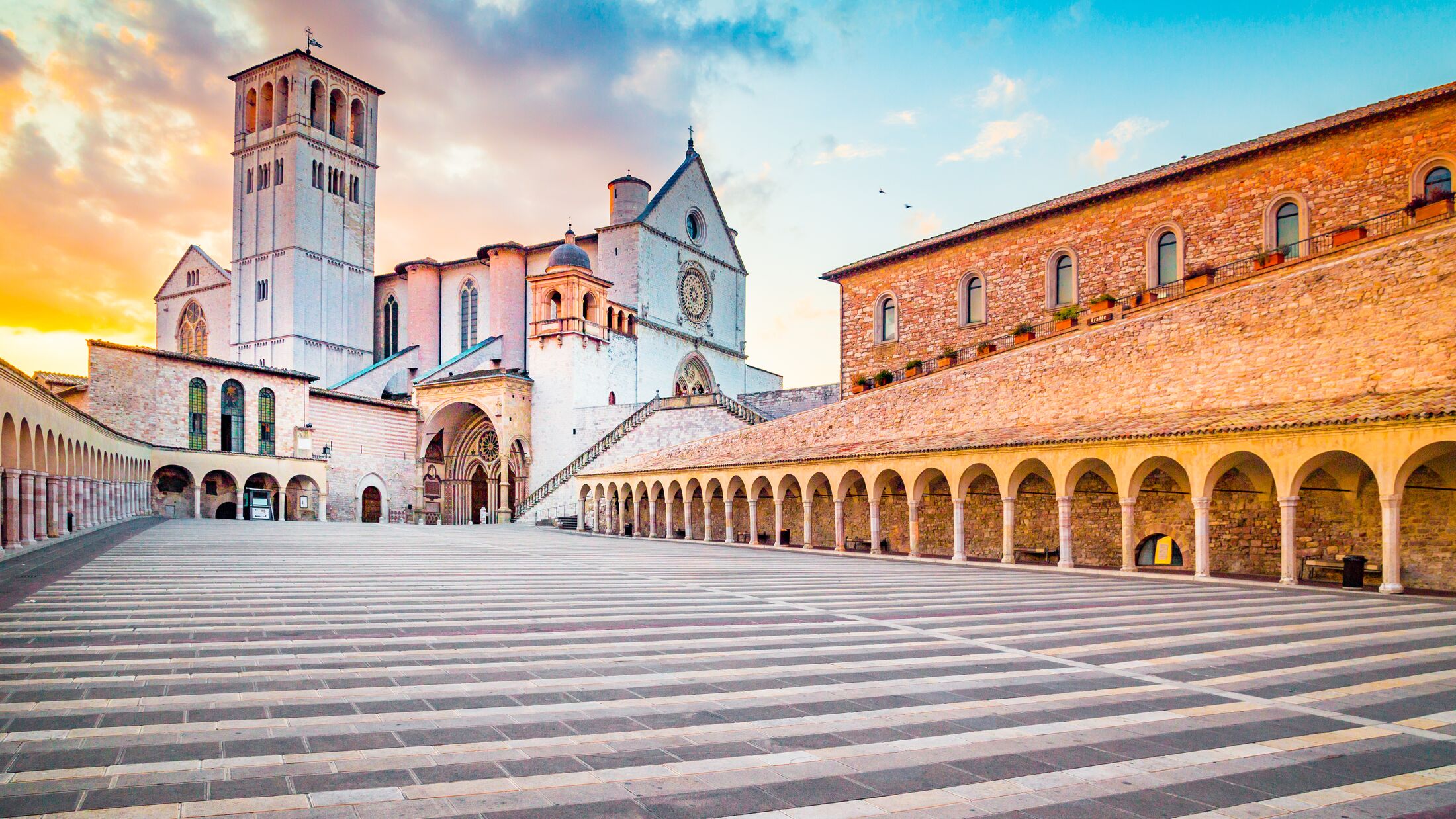 Famous Basilica of St. Francis of Assisi (Basilica Papale di San Francesco) with Lower Plaza at sunset in Assisi, Umbria, Italy