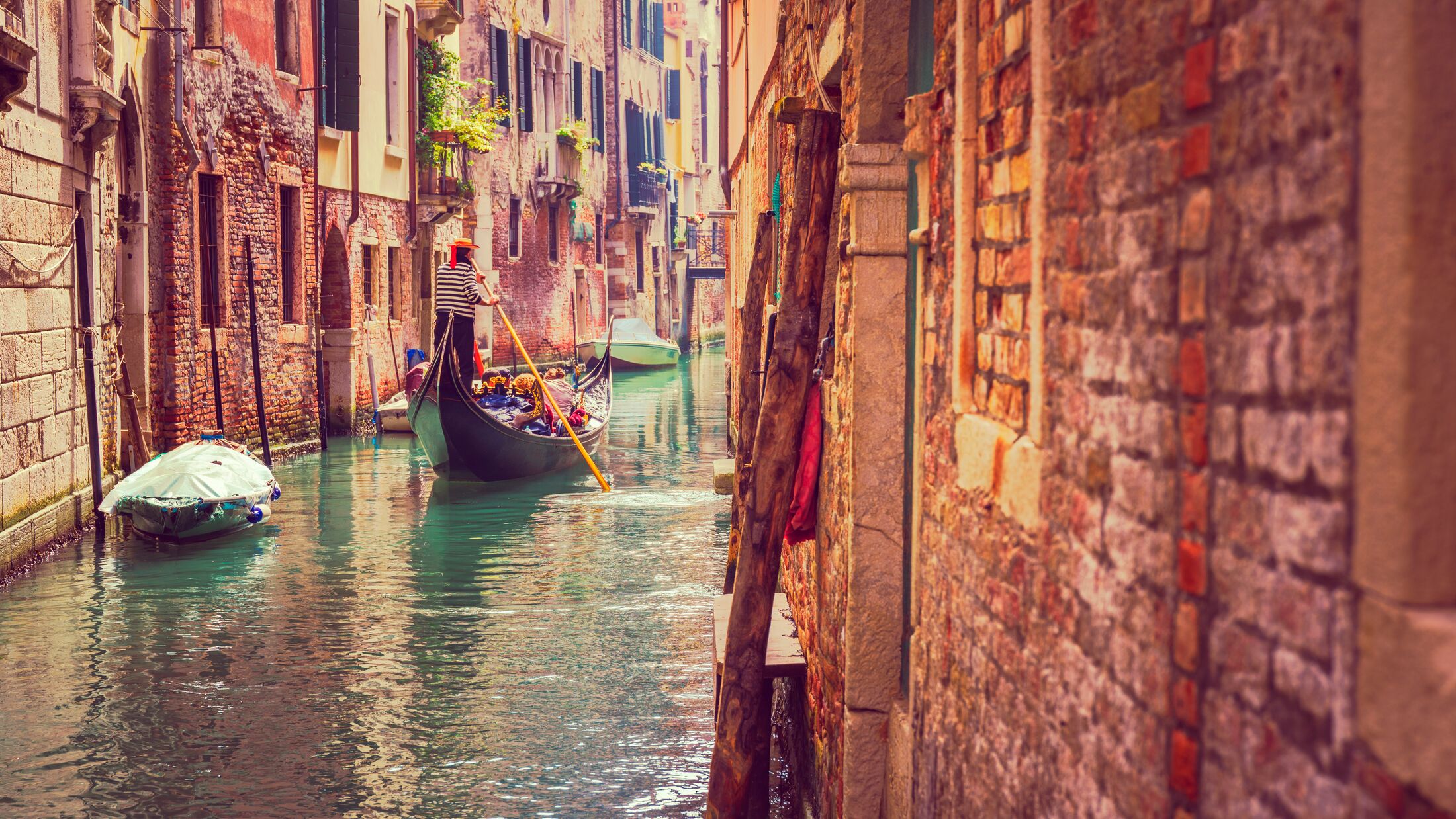 A man rows a Gondola down a narrow canal in Venice
