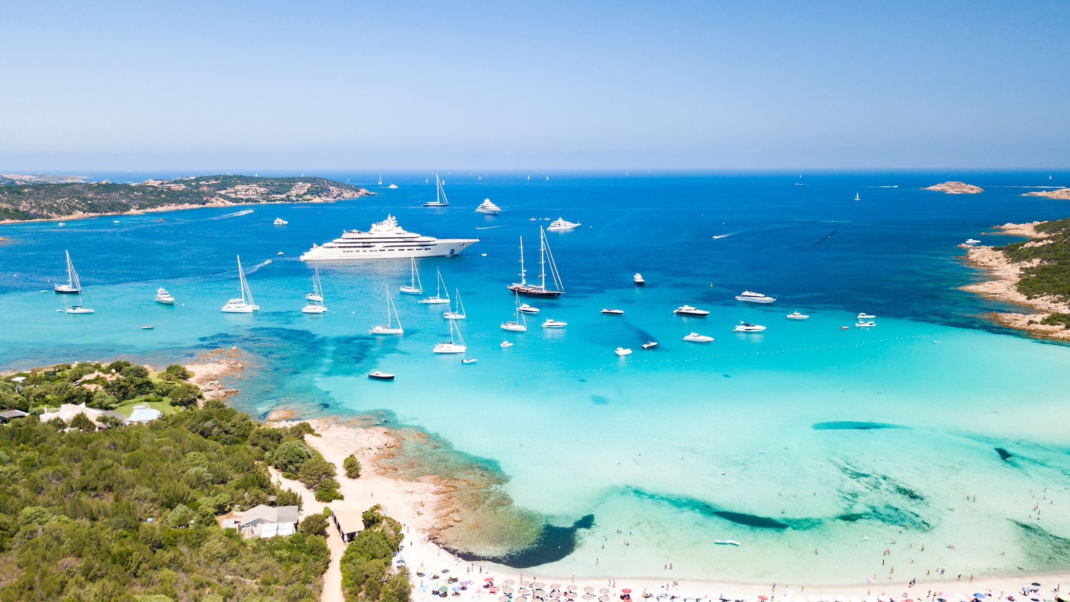 Aerial view of an emerald and transparent mediterranean sea with a white beach and some yachts. Gulf of the Great Pevero, Costa Smeralda, Sardinia, Italy.