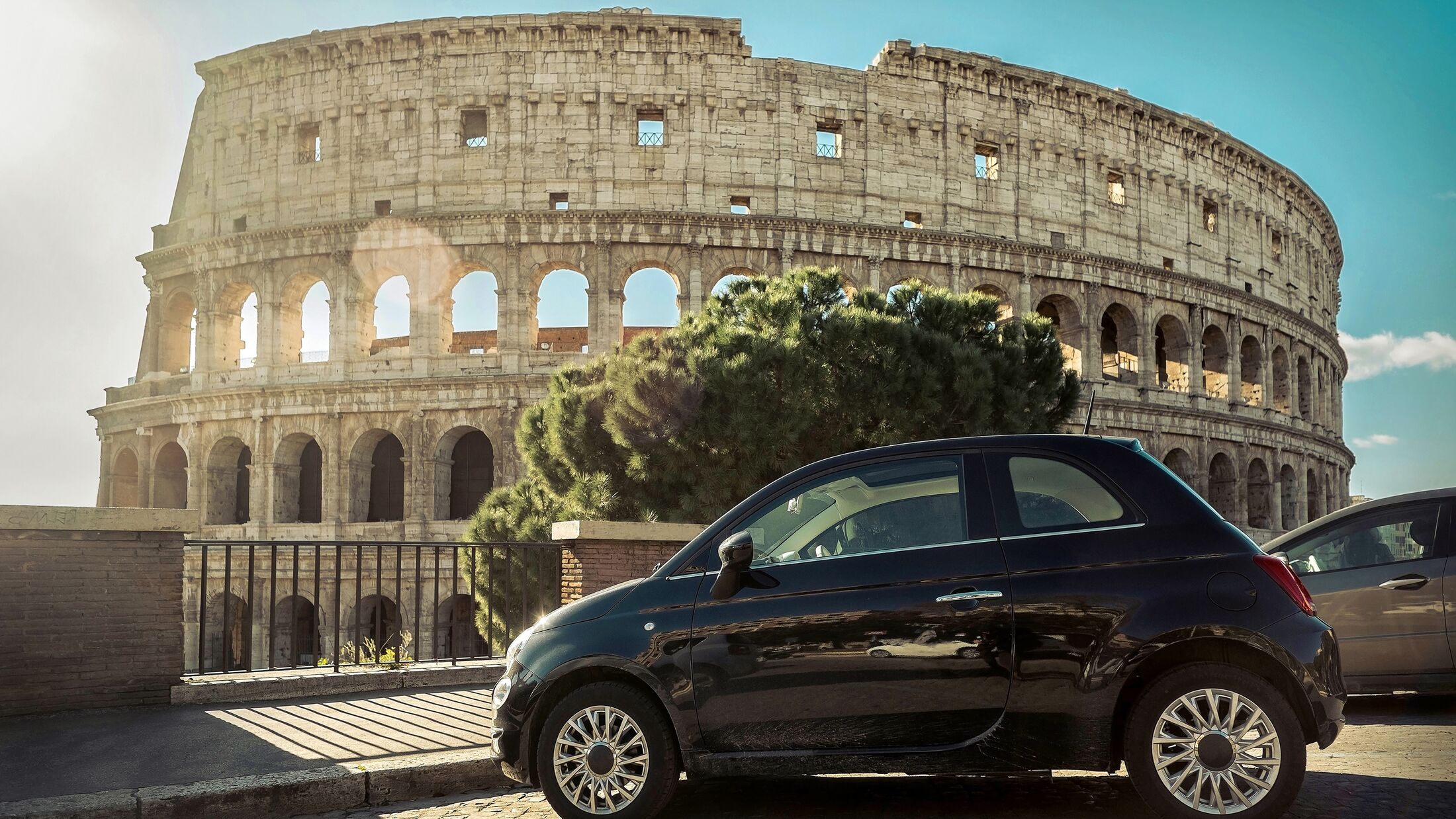 Retro car parking near the Coliseum - one of famous and very popular touristic place of the world, under blue sky at sunny day.