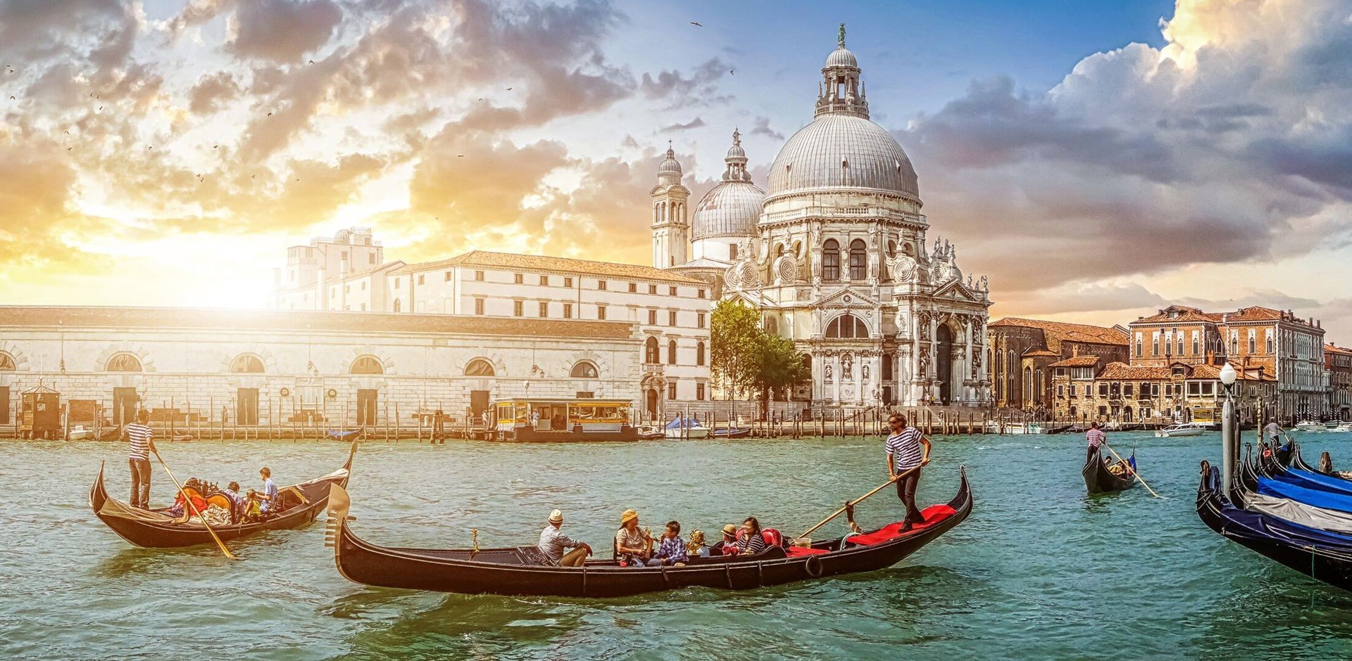 Beautiful view of traditional Gondolas on famous Canal Grande with historic Basilica di Santa Maria della Salute in the background in romantic golden evening light at sunset in Venice, Italy