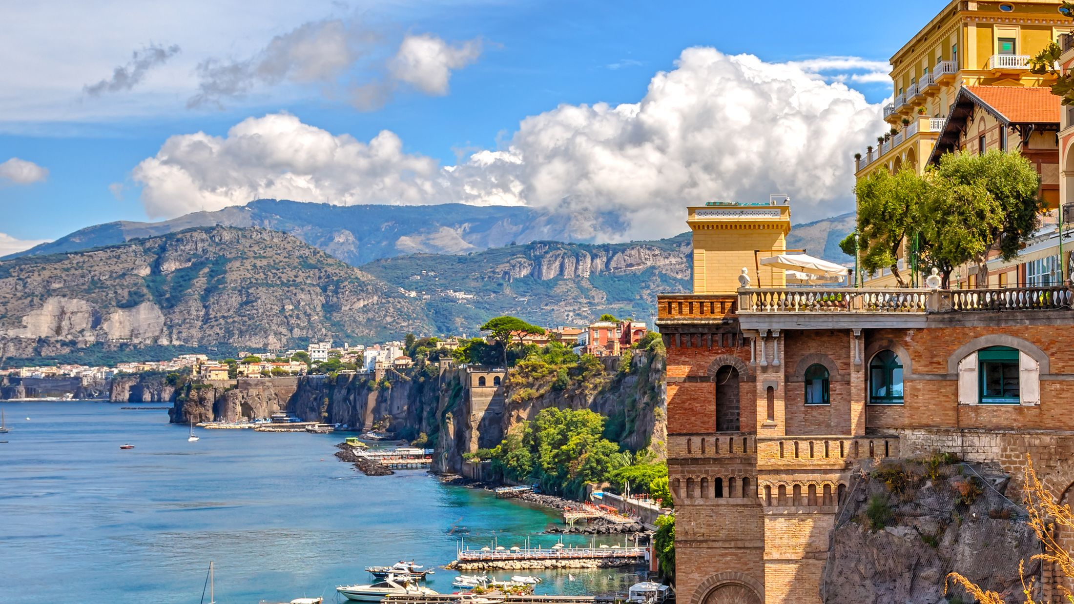 A view of the coast of Sorrento, with a classic building on the right, and mountains in the background