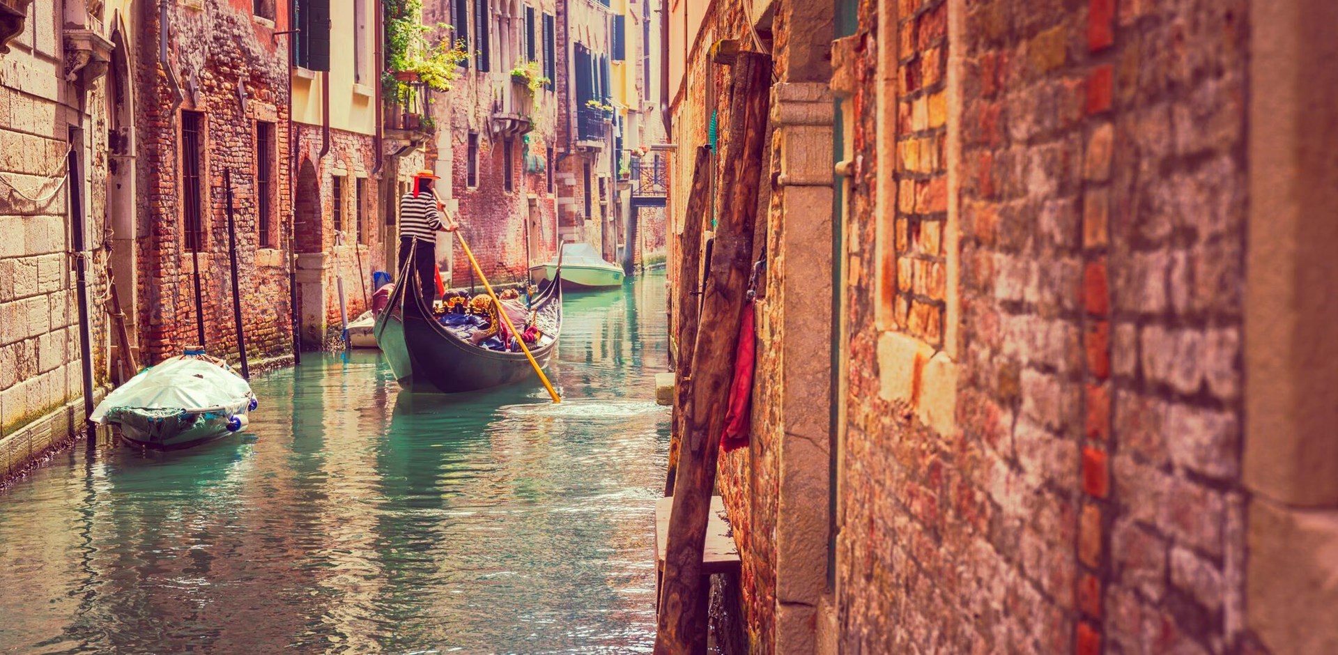 A man rows a Gondola down a narrow canal in Venice