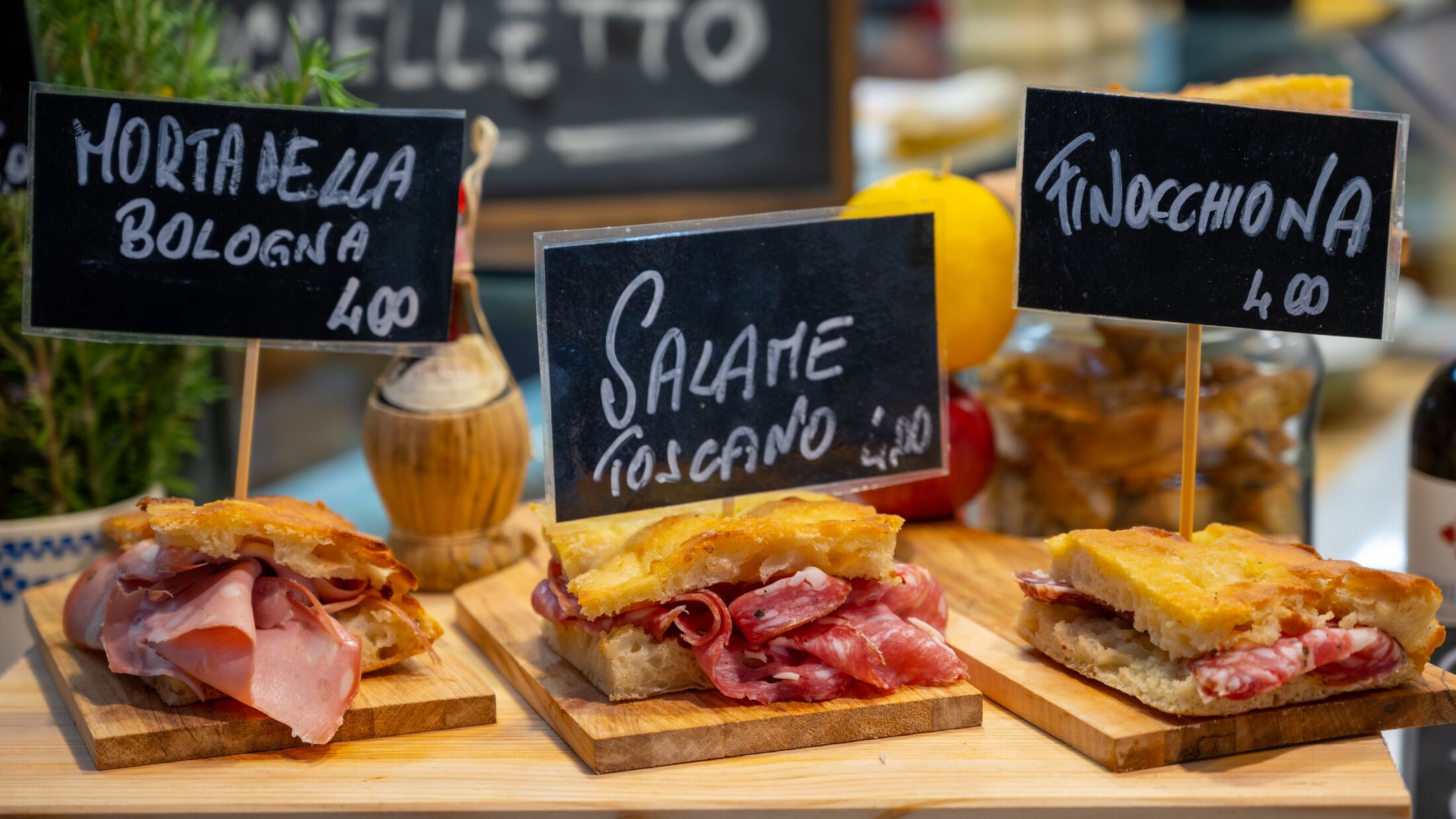 Italian street food, Parma ham sandwiches, bread with cured meats in market in Florence, Italy English translation is: Mortadella from Bologna, Salami from Tuscany and Finocchiona sandwich bread