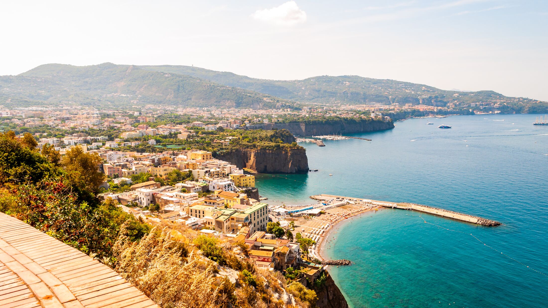 Panorama of high cliffs, Tyrrhenian sea bay with pure azure water, floating boats and ships, pebble beaches, rocky surroundings of Meta, Sant'Agnello and Sorrento cities near Naples region in Italy