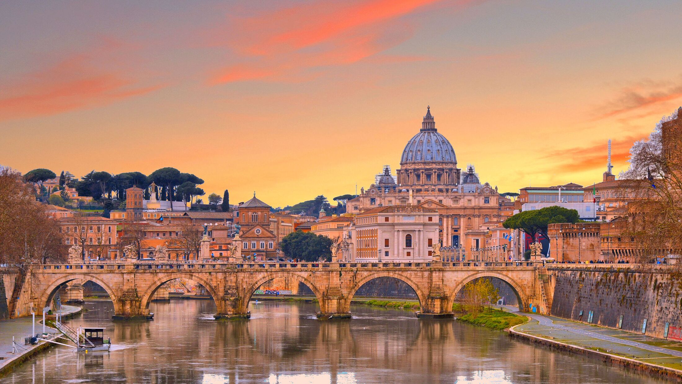 cityscape and panoramic view of old bridge with warm sunset sky water reflections and dome of St. Peters cathedral church with old buildings and architecture in Rome, Italy