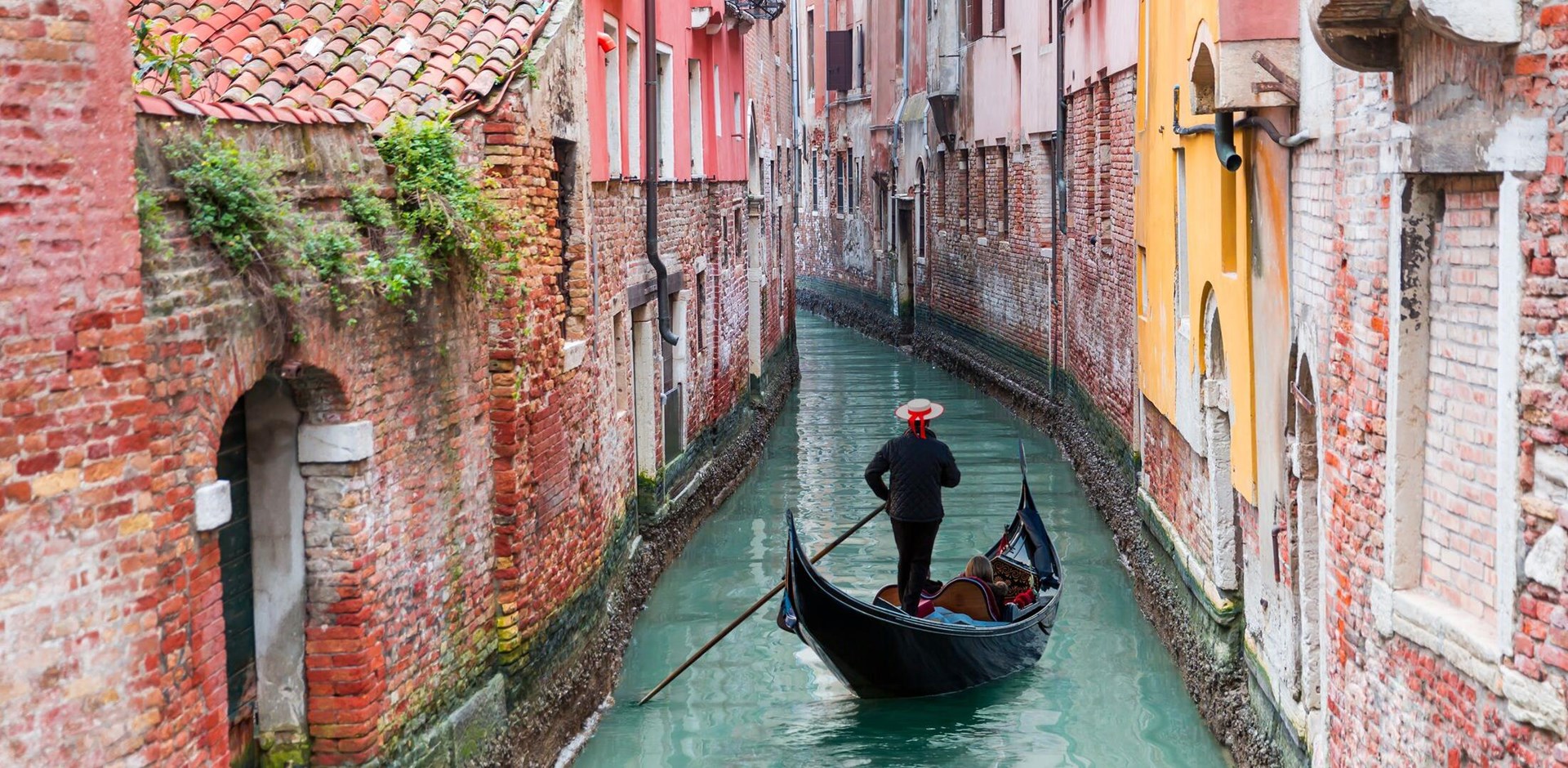 Venetian gondolier punting gondola through green canal waters of Venice, Italy