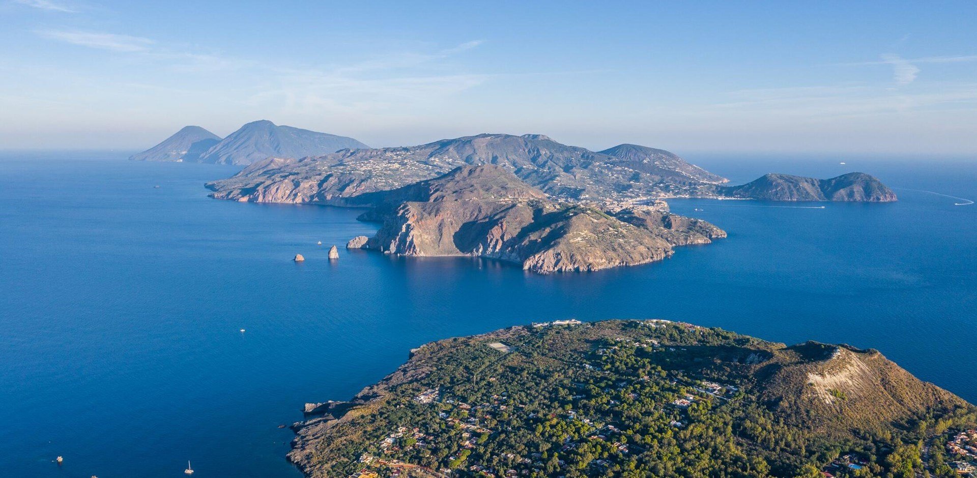 Aerial view photo from flying drone of Panoramic view from the volcano of Vulcano Island in a summer day. The islands of Lipari and Salina are visible in the distance, Aeolian Islands, Sicily, Italy.
