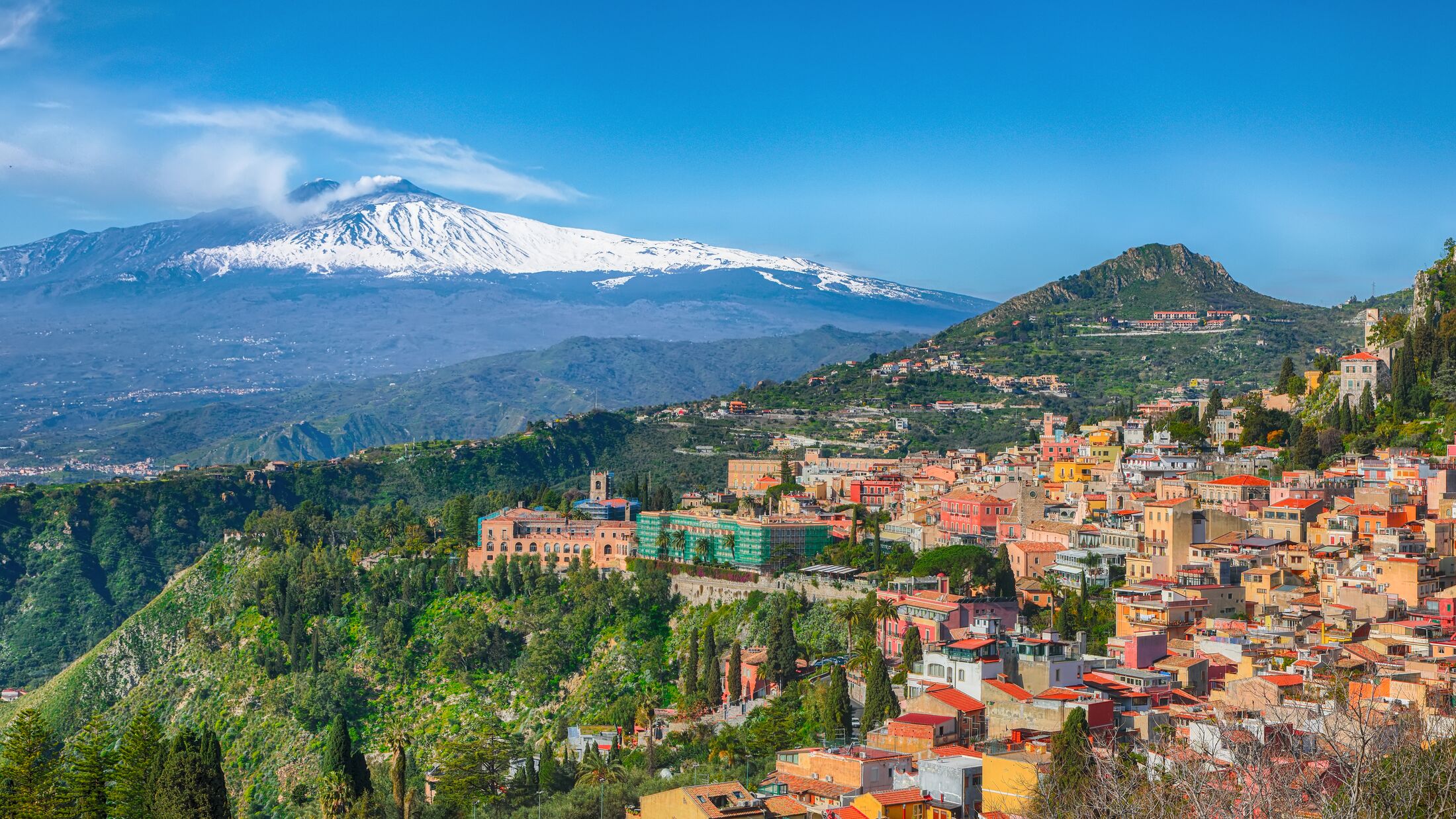 Etna volcano and Taormina town aerial panoramic view. Roofs of a lot of buldings. Smoking snow-capped Mount Etna volcano. Taormina, Sicily, Italy.