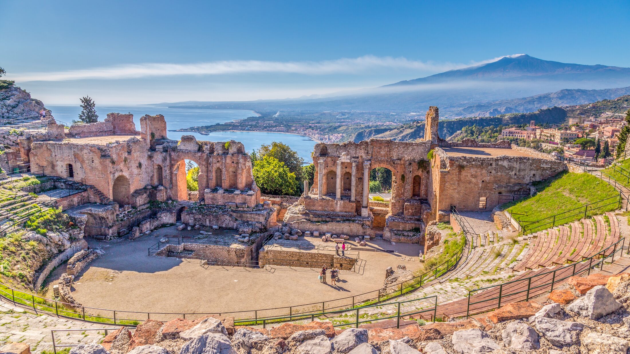 Ruins of the Ancient Greek Theater in Taormina, Sicily with the double smoke tail of the Etna extending over the the Giardini-Naxos bay of the Ionian Sea in the morning sun shine.