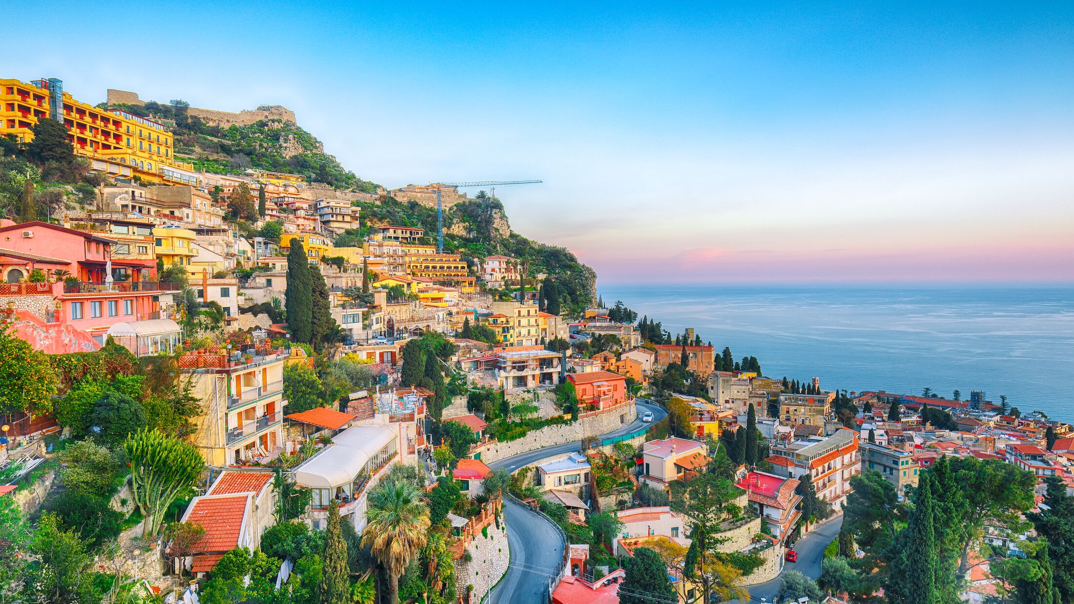Aquamarine blue waters of  sea and fantastic cityscape of Taormina during sunset. Giardini-Naxos bay, Ionian sea coast, Taormina, Sicily, Italy.