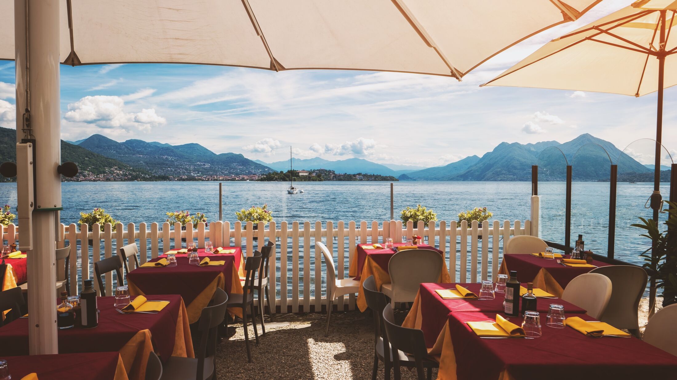 Tables and chairs near water. Mountains at distance. Restaurant in the open air.