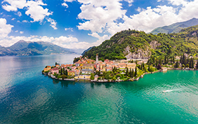Beautifull aerial panoramic view from the drone to the Varenna - famous old Italy town on bank of Como lake. High top view to Water landscape with green hills, mountains and city in sunny summer day.