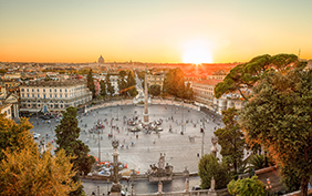 Aerial view of the large urban square, the Piazza del Popolo, Rome at sunset with the fiery orb of the sun dropping below the horizon above the rooftops of the historical buildings