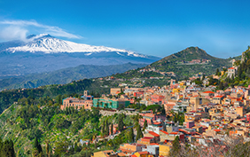 Etna volcano and Taormina town aerial panoramic view. Roofs of a lot of buldings. Smoking snow-capped Mount Etna volcano. Taormina, Sicily, Italy.