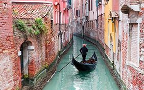 Venetian gondolier punting gondola through green canal waters of Venice, Italy