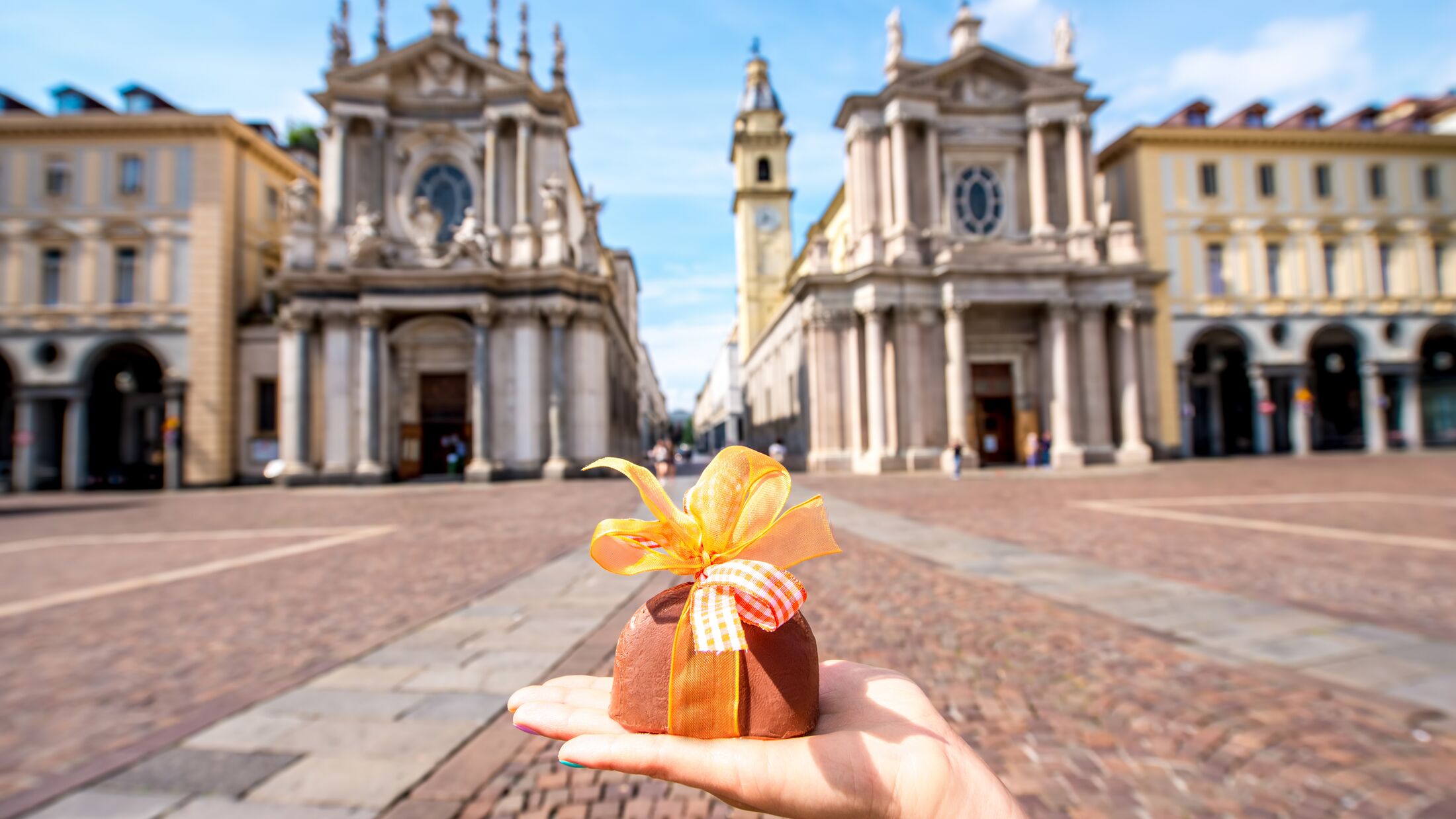 Holding italian chocolate with bow on Turin city background. Turin in Piedmont region in Italy is famous of its chocolate making