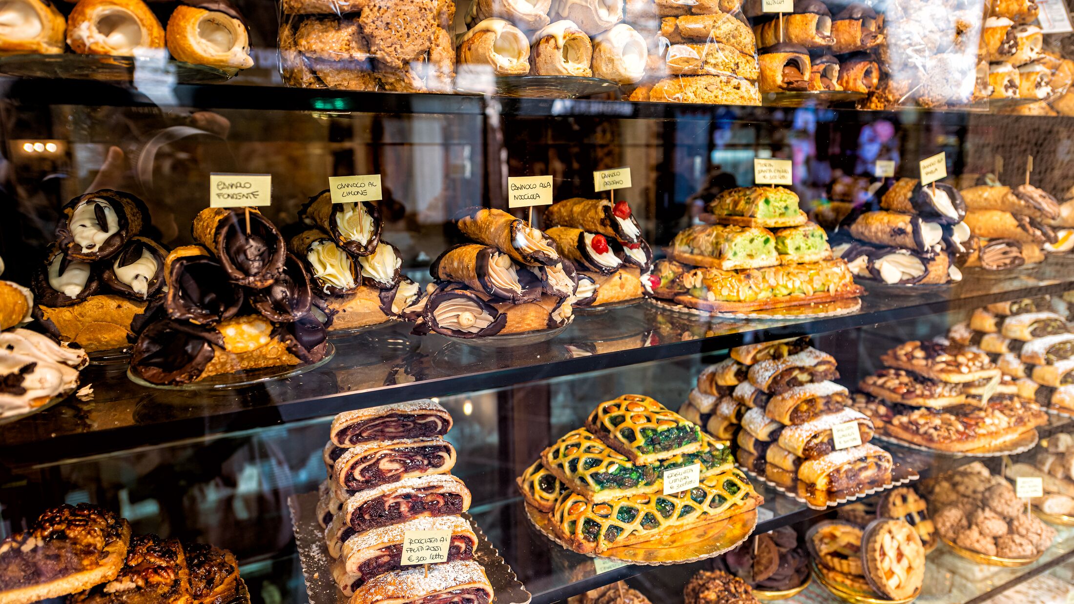 Pastry bakery store shop in Assisi, Umbria Italy selling dessert chocolate cannoli, rocciata cakes and pies with price tags through retail display glass window