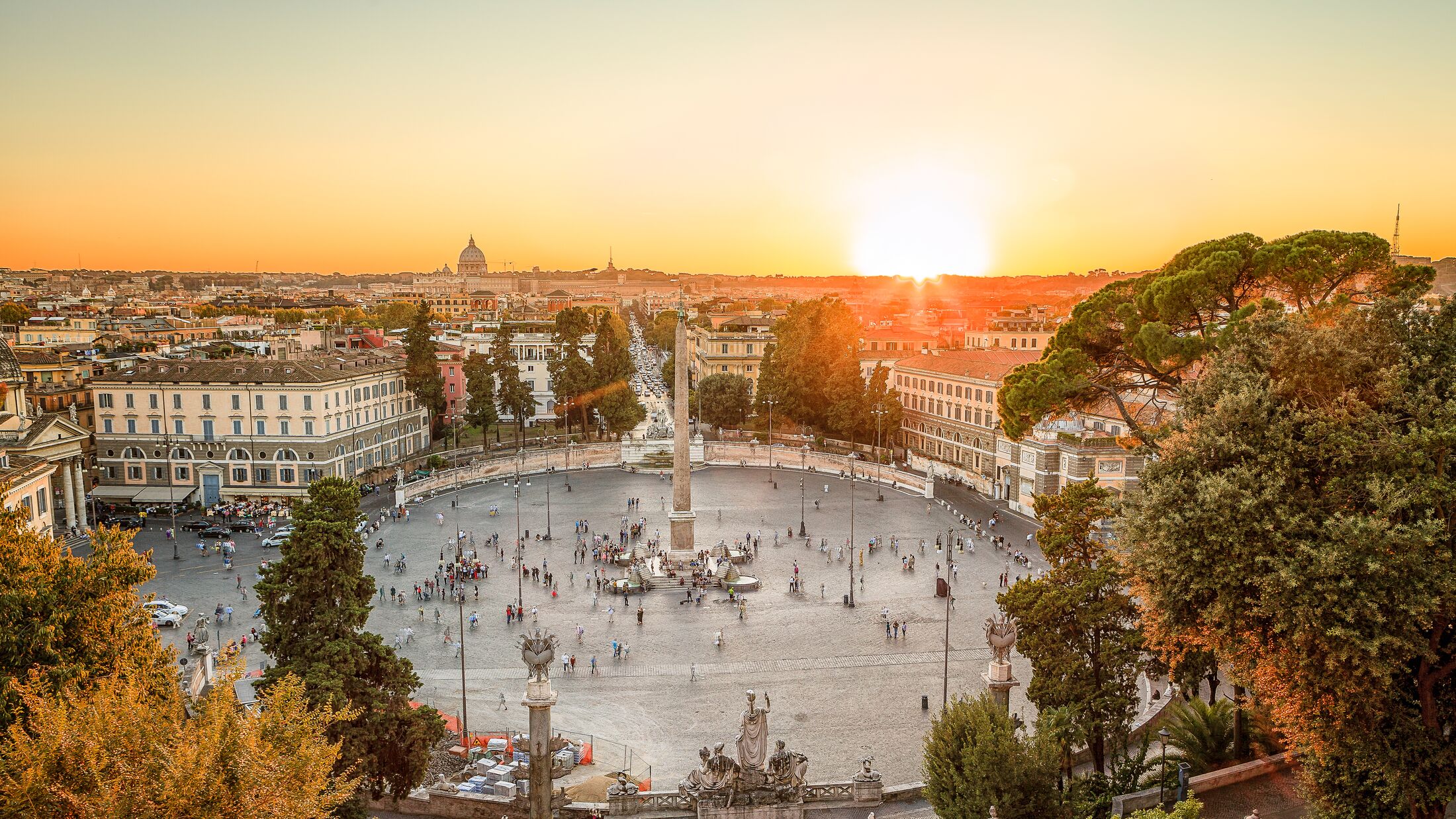 Aerial view of the large urban square, the Piazza del Popolo, Rome at sunset with the fiery orb of the sun dropping below the horizon above the rooftops of the historical buildings