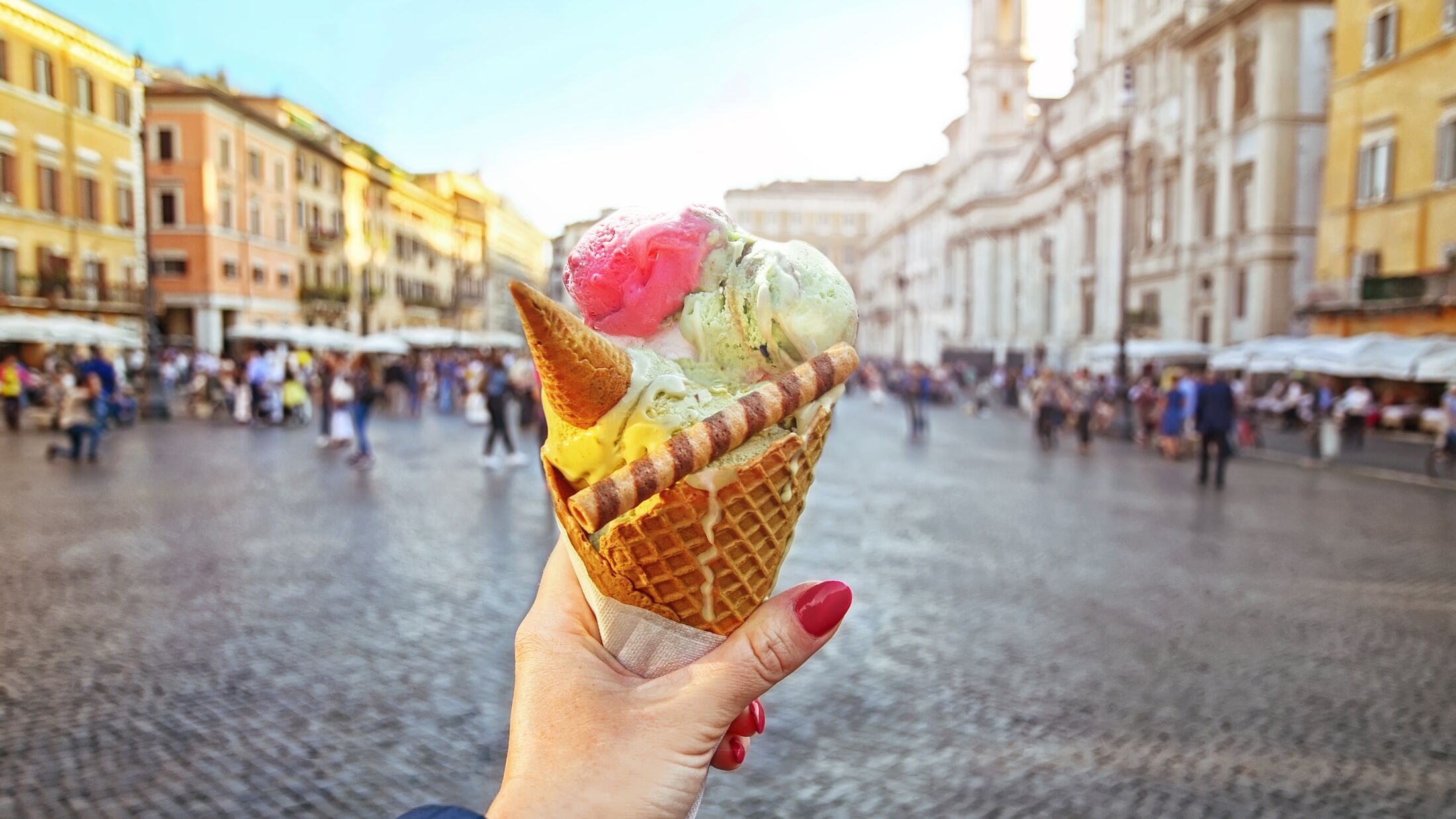 Italian ice - cream cone held in hand on the background of Piazza Navona in Rome , Italy