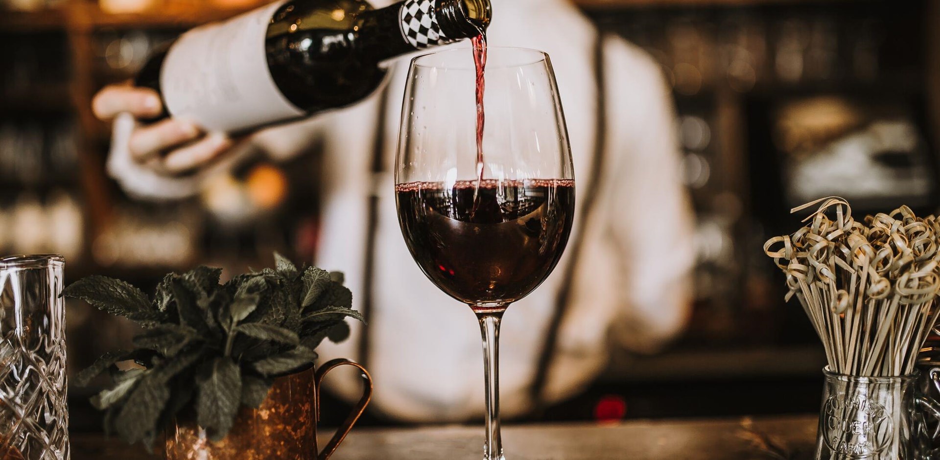 Bartender pouring red wine from a bottle in a wine glass, selective point of view on a wine glass
