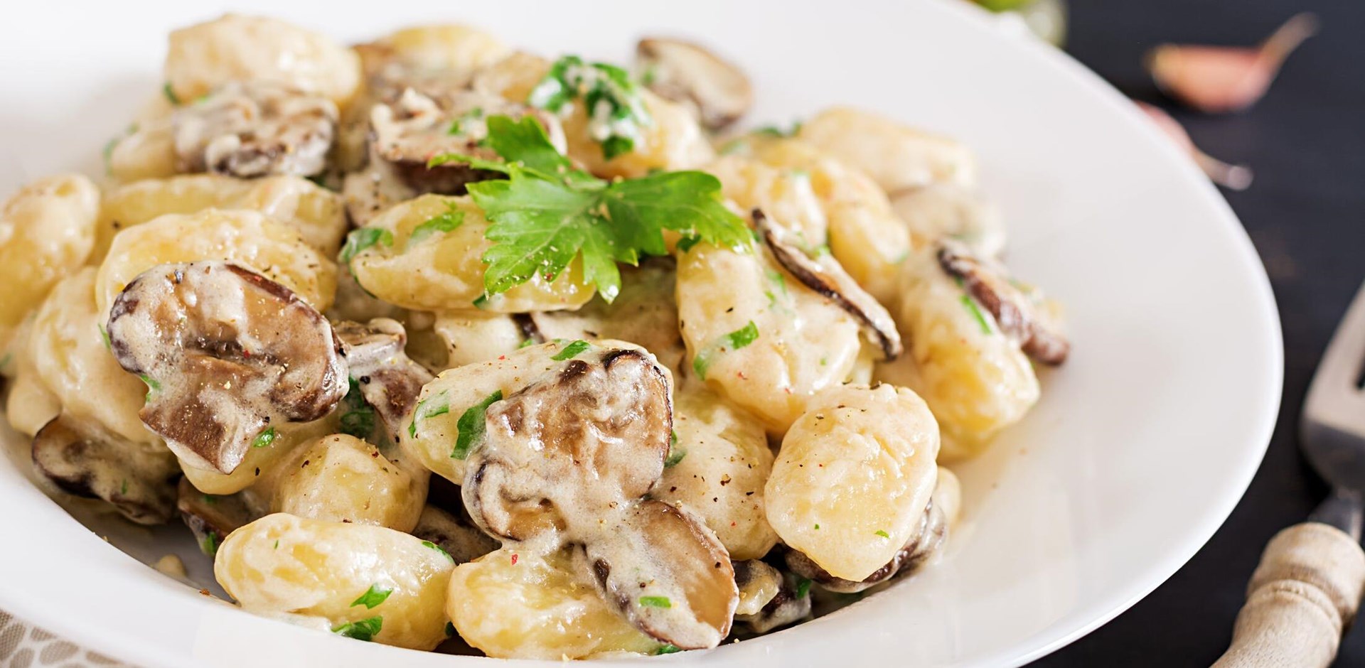Gnocchi with a mushroom cream sauce and parsley  in bowl on a dark background