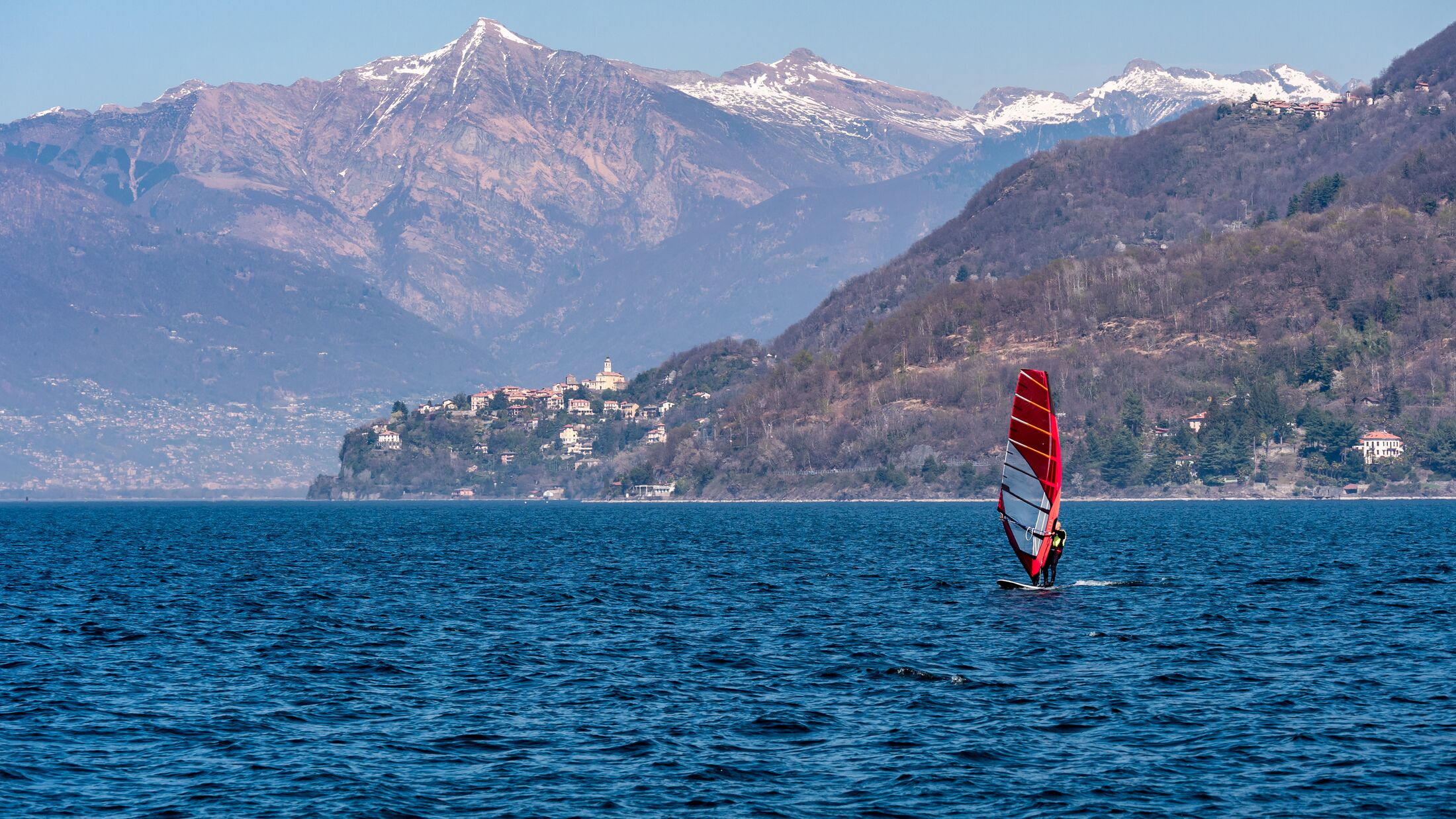 Image of surfer on the lake maggiore with city and alps with snow peaks in the background